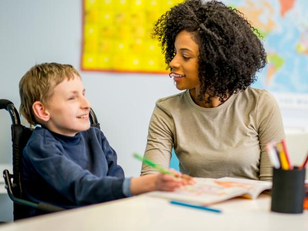 An adult talking to a child in a wheelchair, sat at a table
