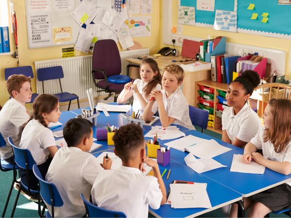 Eight children sat around a table in a classroom having a discussion