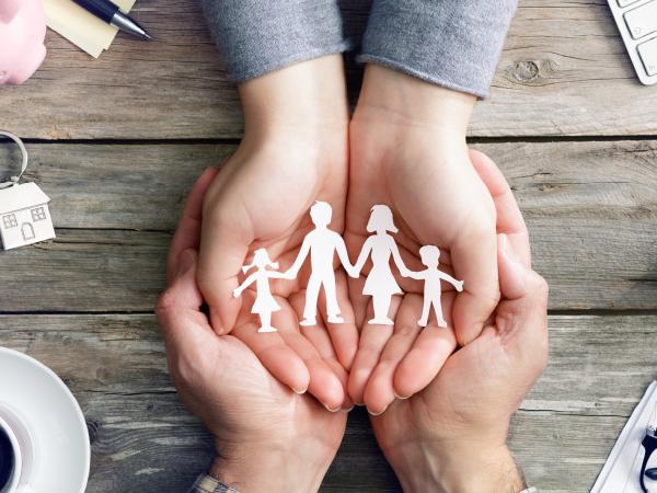 A child's hands cupped in a adult's hands, resting on a table, with a cardboard cut out of a family resting inside the hands