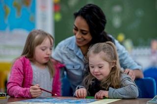 Two children with special needs drawing, with an adult interacting with them